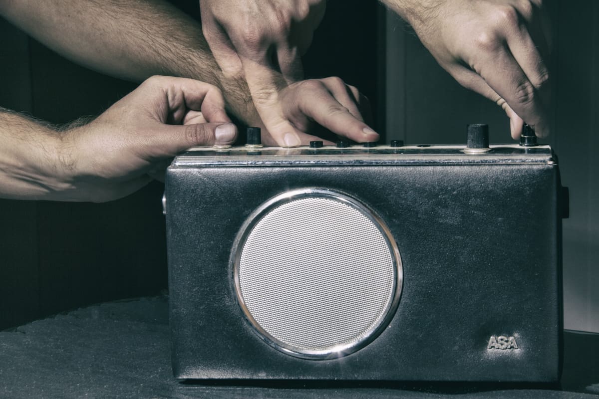 Neljä kättä säätää vanhan ASA-radion nappuloita.