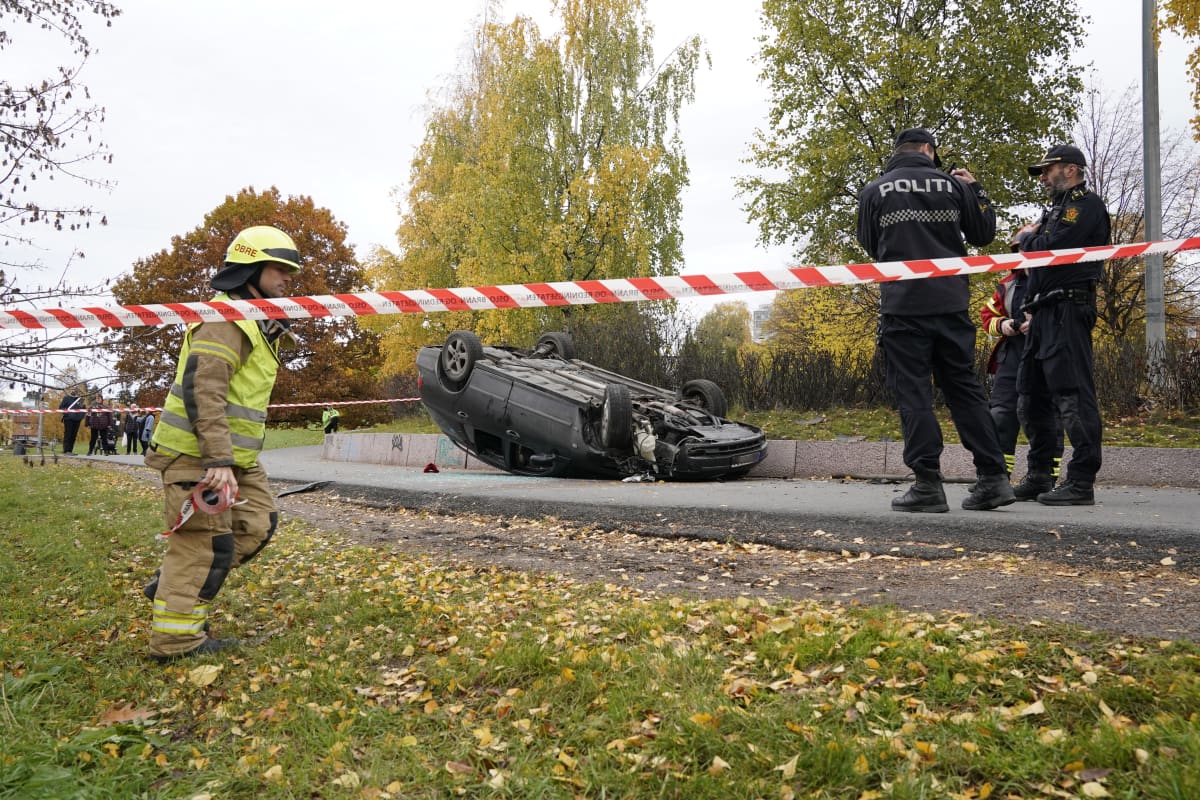 Katolleen kääntynyt auto. Ympärillä palomies ja poliiseja.