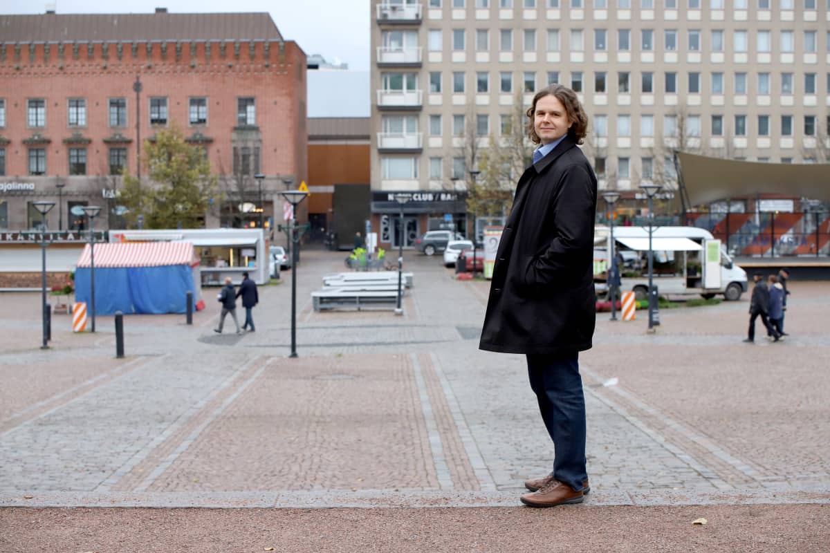 Mies katsoo kameraan Hämeenlinnan torin laidalla.
