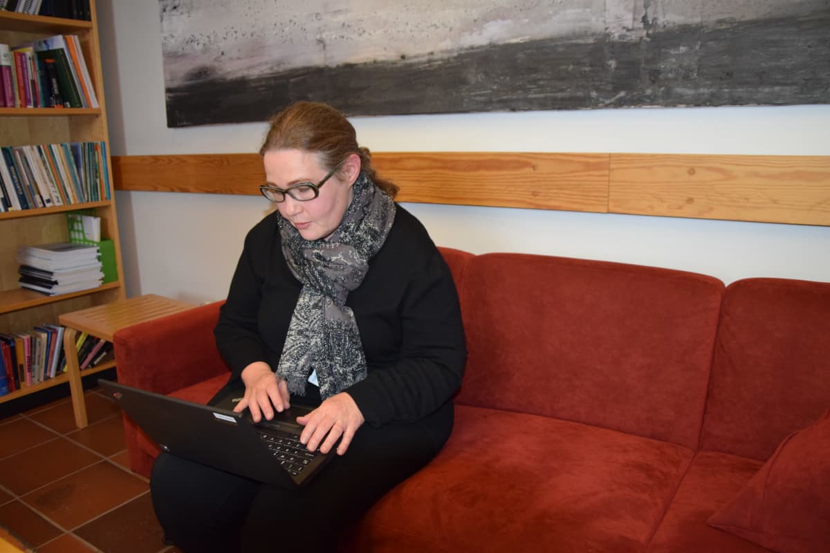 Nainen istuu sohvalla ja näpyttelee tietokonetta.