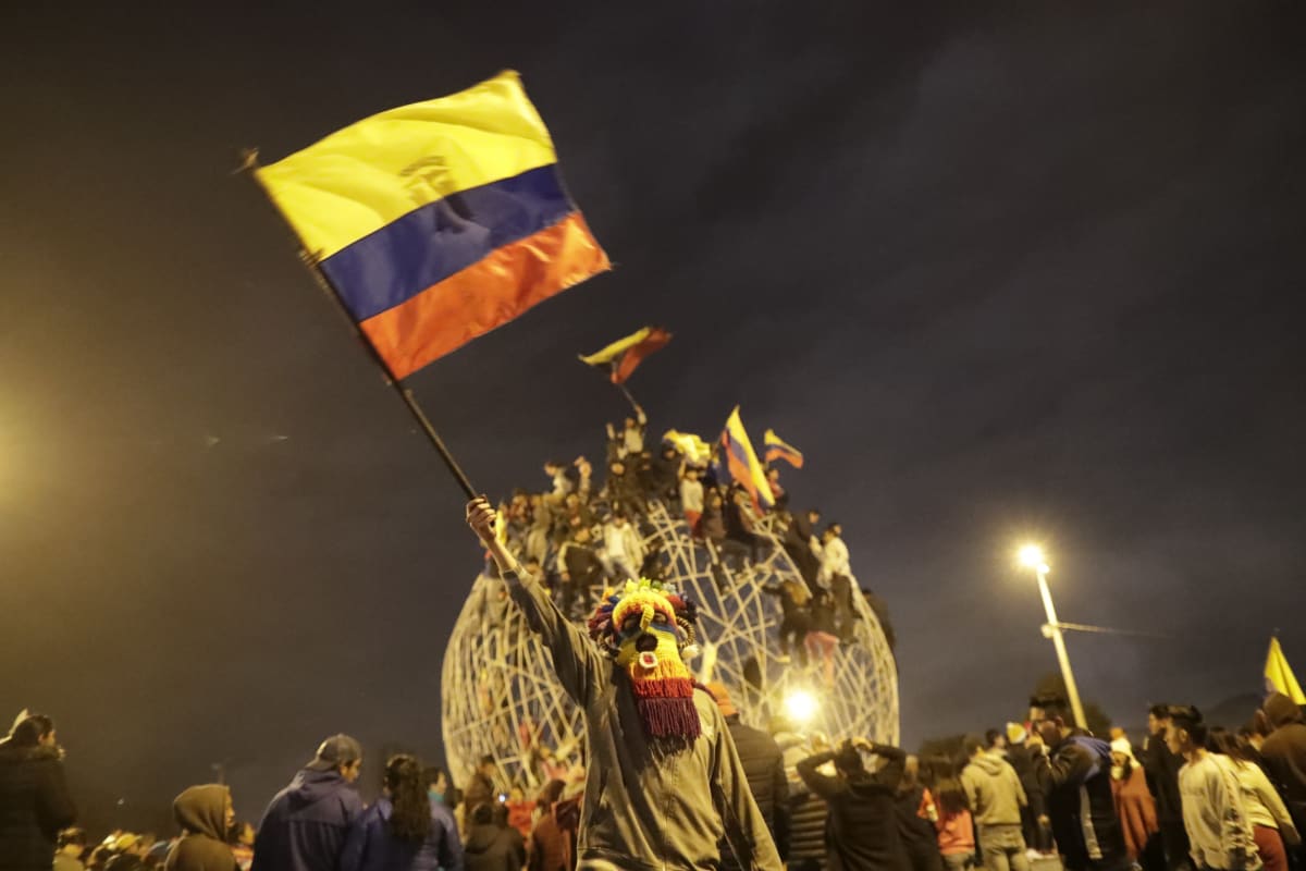 Värikkäällä naamiolla naamioitunut ihminen heiluttaa Ecuadorin lippua.