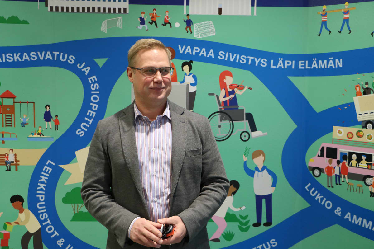 Man i kostymjacka står framför mural som avbildar utbildning och fostran