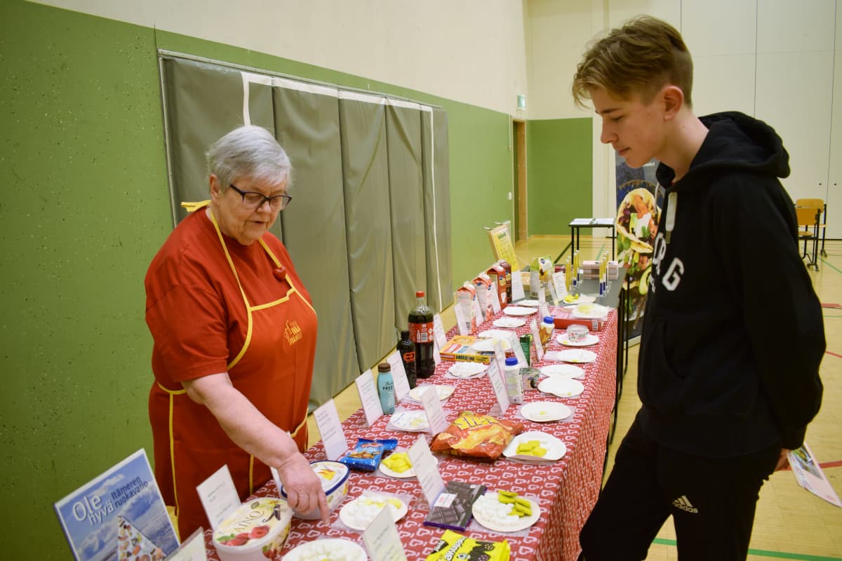Nainen esittelee pojalle herkkujen sokeri- ja rasvapitoisuuksia.
