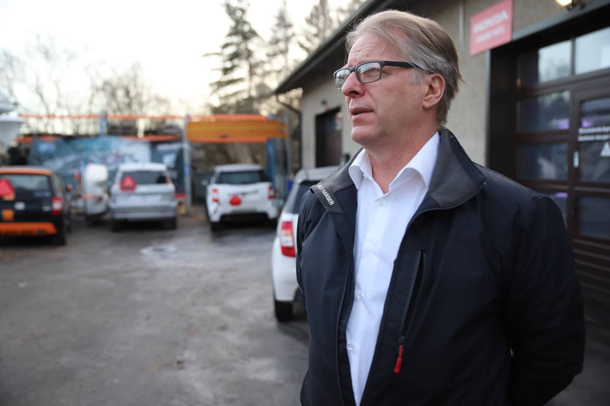Juha Dahlman seisoo ulkona. Piha on täynnä mopoautoja.