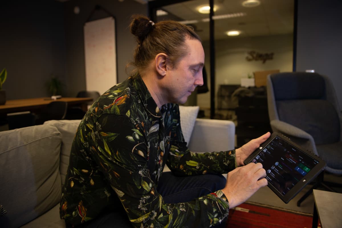 Singa yhtiön Luca Gargano istuu toimistossa sohvalla ja pitää kädessään tietokonetablettia selaten sillä Singa karaokeohjelman luetteloa musiikkikappaleista.