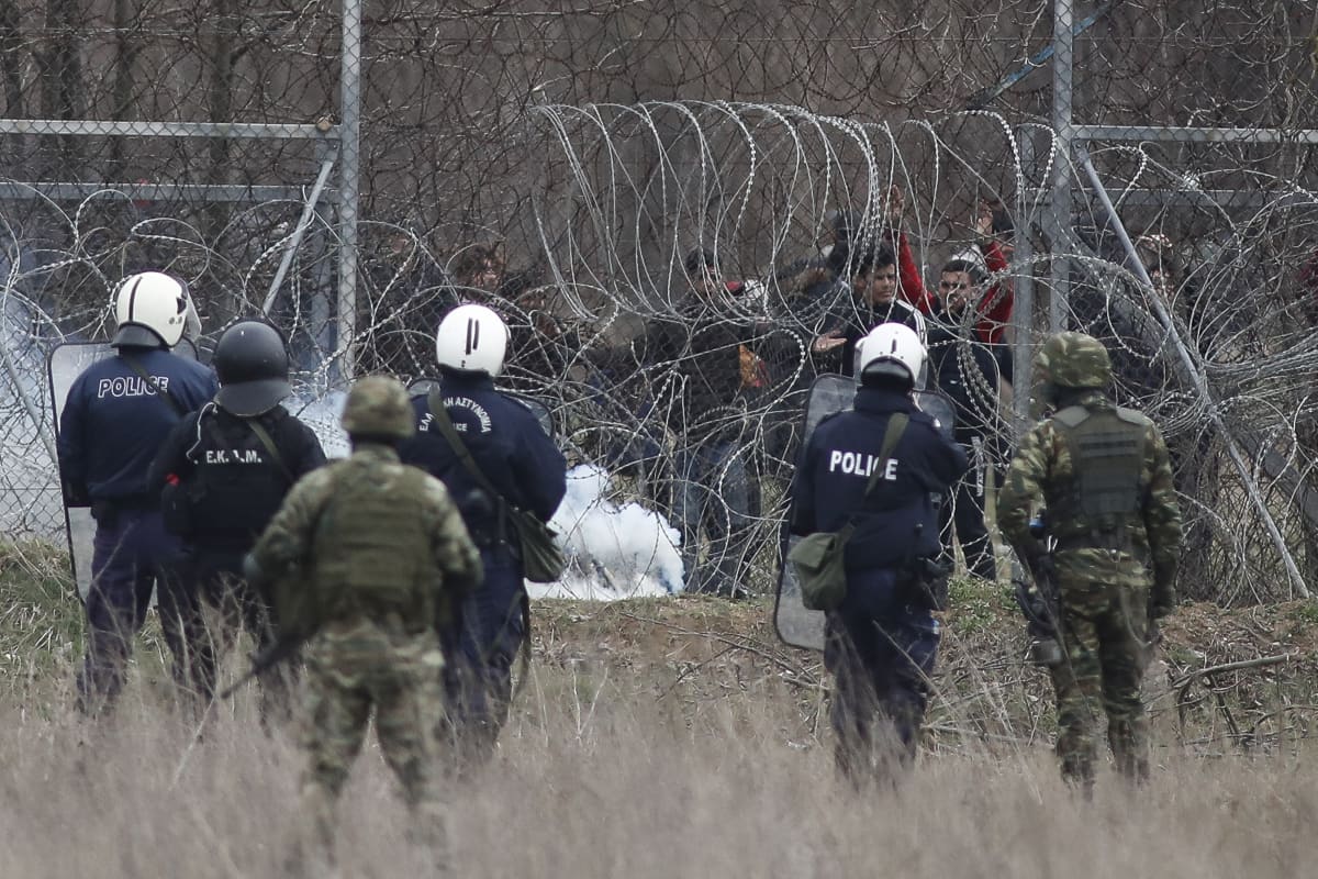 Kreikkalaisia poliiseja piikkilanka-aidan edessä, toisella puolella Turkista pyrkiviä siirtolaisia.
