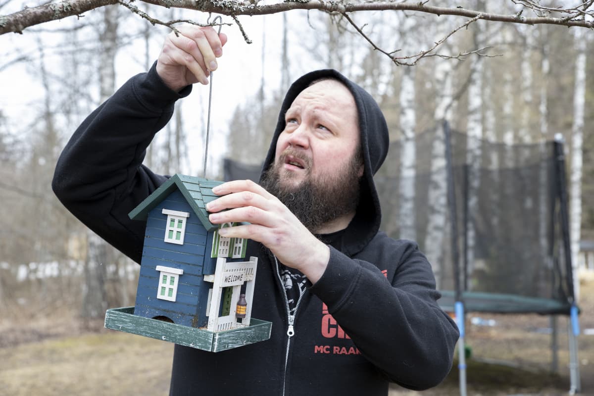 Muusikko Petja Turunen asettelee lintulautaa puunoksaan.