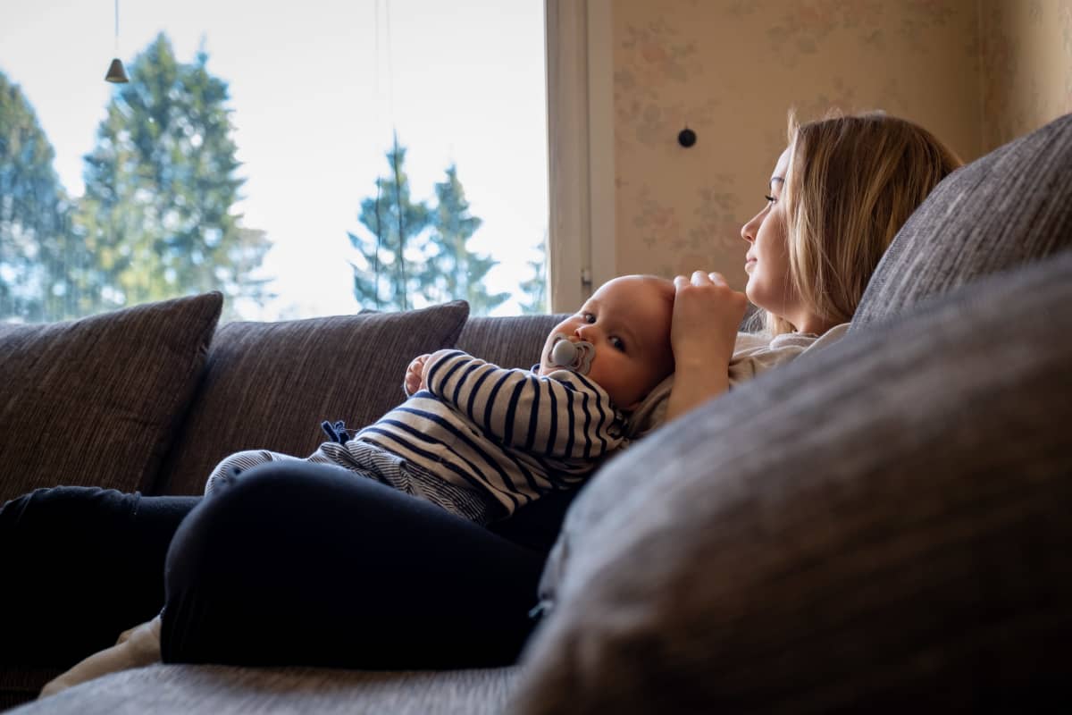 Niina Mantere istuu sohvalla sylissään 10kk ikäinen Oliver Tojkander.