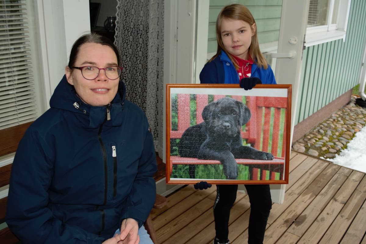 Kirsi ja Aino Saari näyttävät koira-aiheista palpeliä, joka on kehyksissä