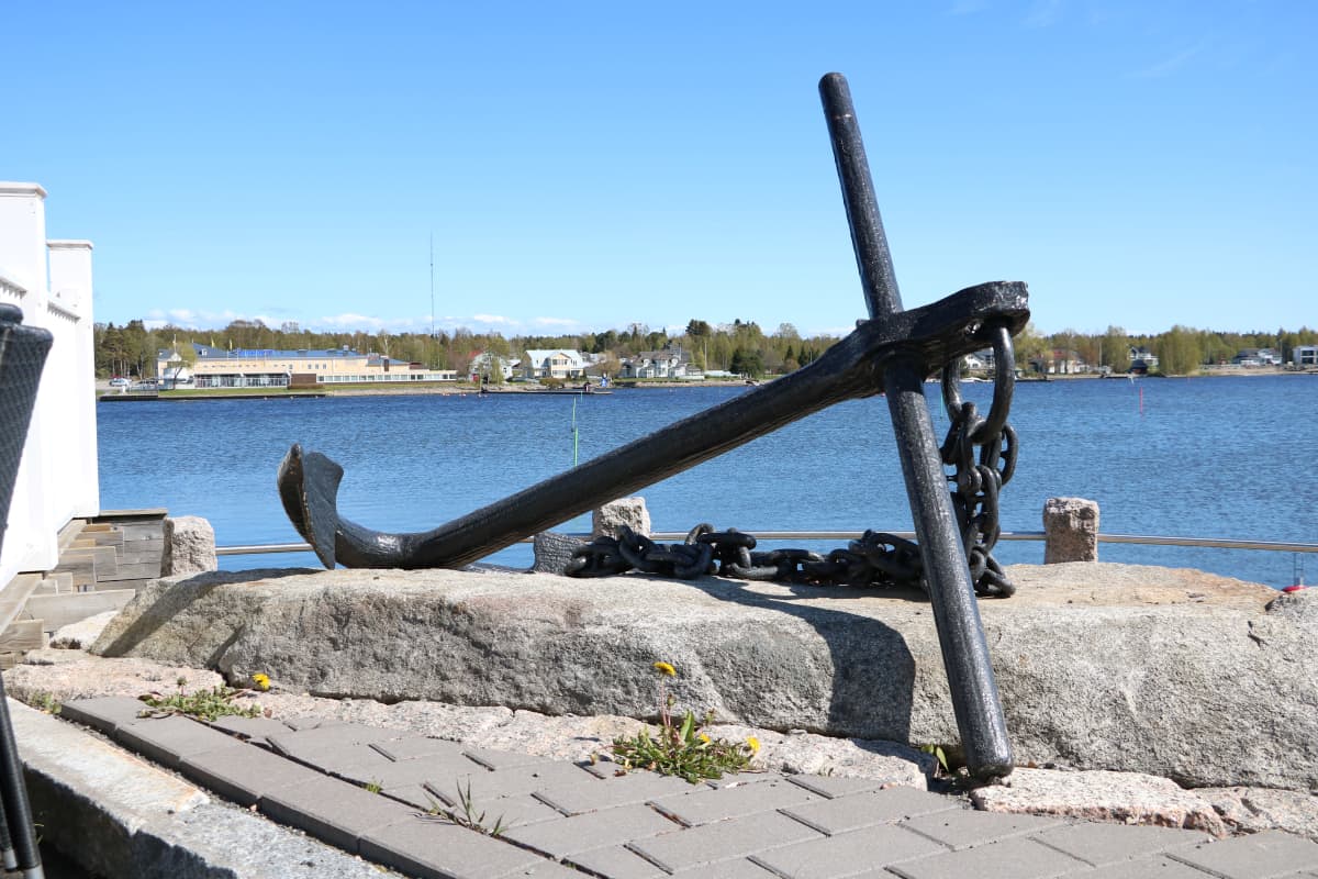 Ett stort svart ankare ligger på en sten intill havet.