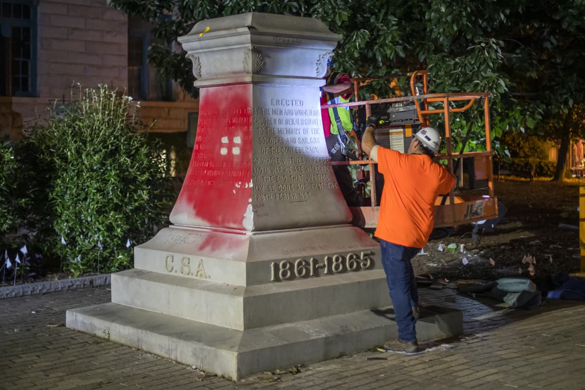 Kaksi työntekijää punaisella maalilla tuhritun monumentin luona.