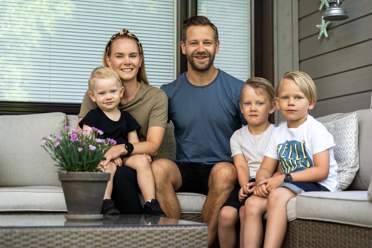 Perhekuva. Mies, nainen ja kolme 3-7-vuotiasta poikaa istuvat ulkona polyrottinkisohvalla ja katsovat hymyillen kameraan.
