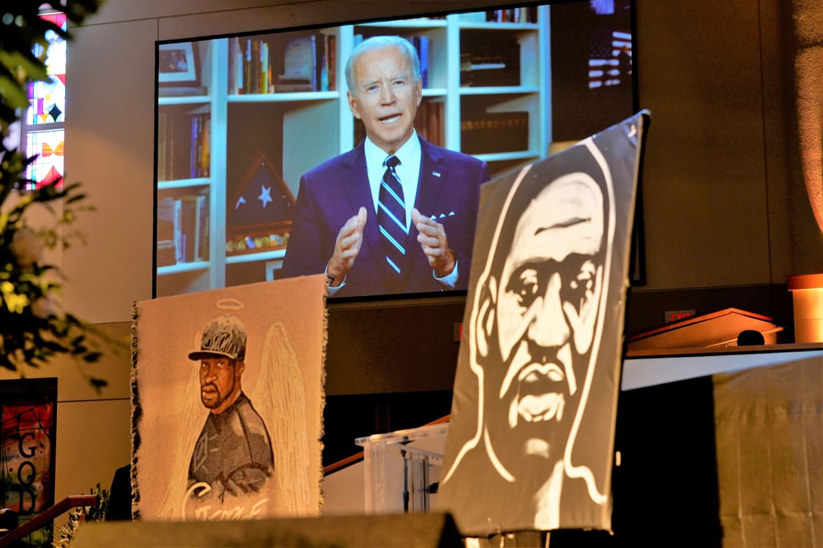 Biden puhuu taustalla näkyvällä televisioruudulla. Etualalla on kaksi maalausta George Floydista. Toinen on mustavalkoinen tyylitelty kuva hänen kasvoistaan. Toisessa hänelle on maalattu enkelin siivet ja sädekehä.
