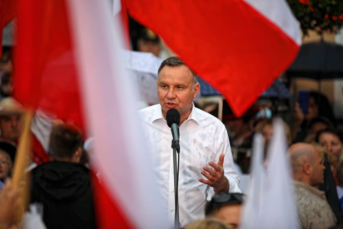 Andrzej Duda puhuu paitahihasillaan mikrofoniin. Etulalalla liehuu Puolan lippuja.