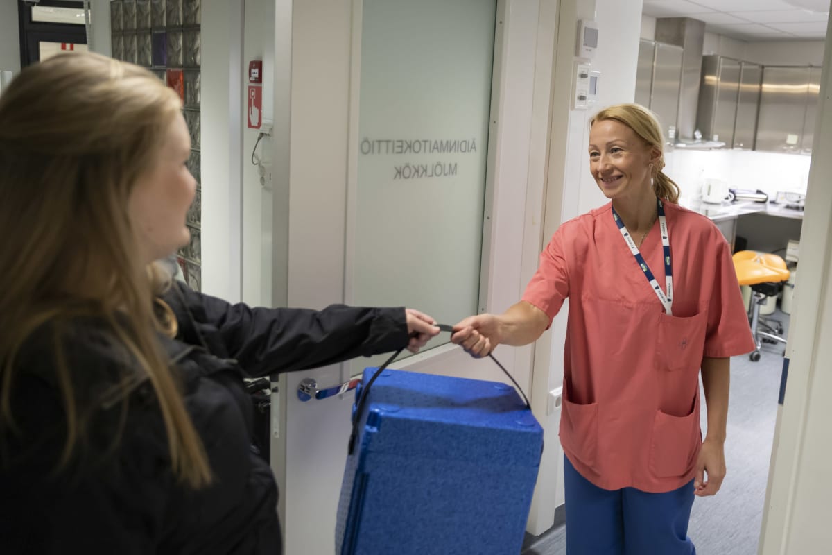 Lähihoitaja ottaa vastaan sinisen kylmälaukun ovensuussa.