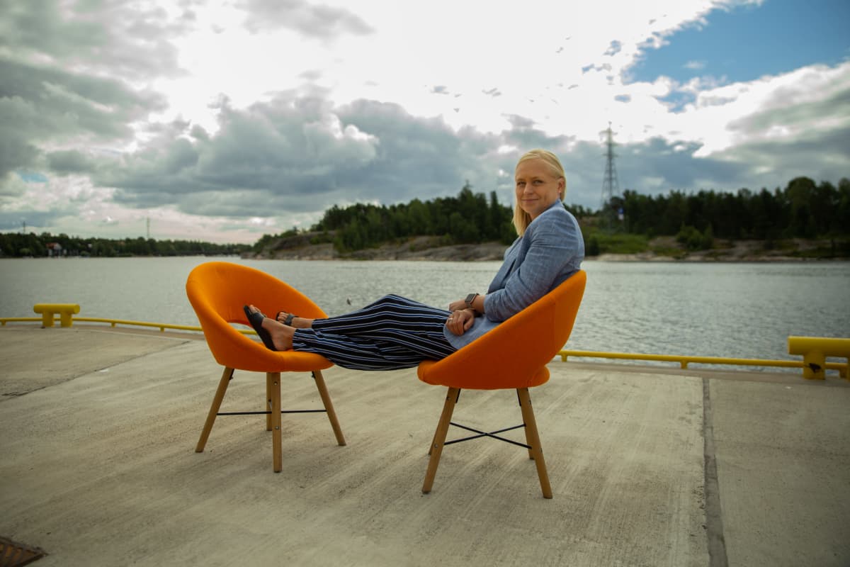 Elina Lepomäki istuu 8 minuuttia -ohjelman oranssilla tuolilla laiturilla Helsingin Kalasatamassa