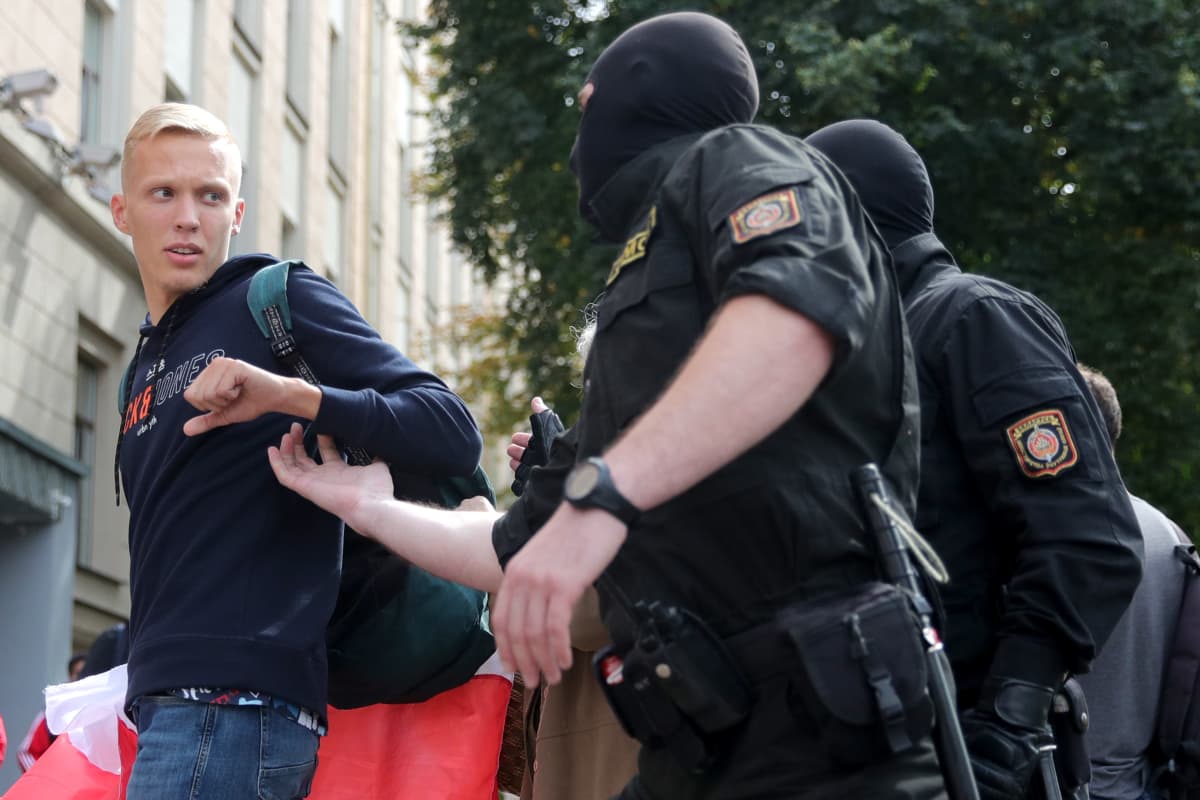 Naamioitunut poliisi ottamassa kiinni nuorukaisen käsivarresta.