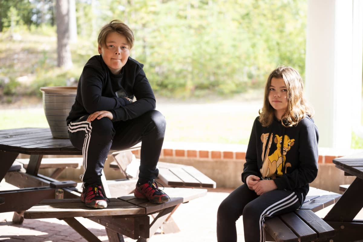 Oppilaat Roope Lauronen ja Janessa Korva istuvat Leivolan koulun takana