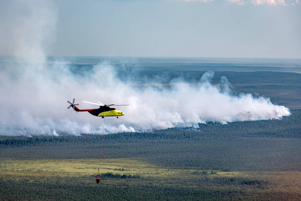 Helikopteri lentää suuren savuavan alueen yllä.
