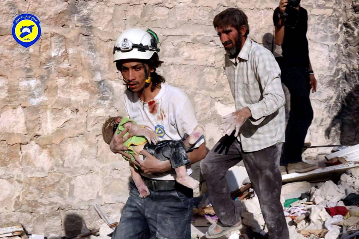 Avustustyöntekijä kuljettaa lasta turvaan Aleppossa.