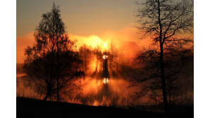 Aurinko nousee usvaisen maiseman takaa.