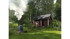 Punainen saunarakennus ja hyöryävä pata sen pihalla.