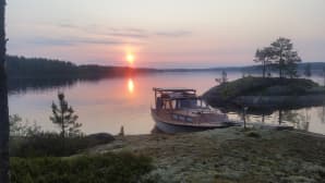 Vene saaren rannassa. Taustalla auringonnousu.