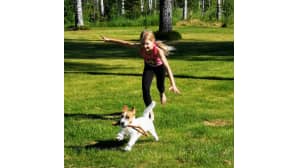 Koira ja tyttö juoksevat nurmikolla.