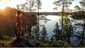 Lapsi katselee tyyntä järveä korkean mäen päältä.