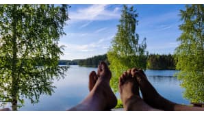 Kahdet paljaat varpaat ja kesäinen järvimaisema.