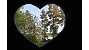 Kesäinen mökkiranta sydämen muotoisen reiän läpi nähtynä.