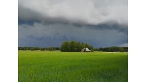 Vihreä peltomaisema jonka takana oleva taivas on tummanpuhuva ja raskas ukkospilvistä.