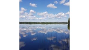 Taivasta peilikirkkaasti heijastava järvimaisema.
