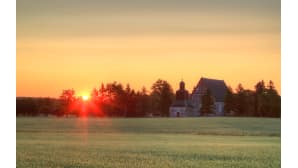 Aurinko värjää punaiseksi vanhan kivikirkon viereiset puiden latvat.