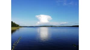 Korkea, valkoinen pilvi muuten tyynen järvimaiseman keskellä.