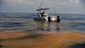 Kalastajat katselevat vedessä kelluvaa öljyä