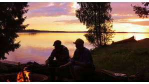 Miehiä iltanuotiolla auringon laskiessa.