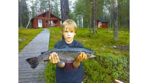 Poika pitää taimenta käsissään.