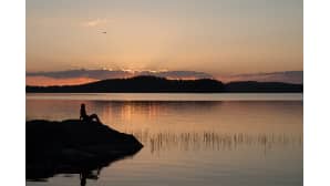 Hahmo ihastelee auringonlaskua rantakalliolla
