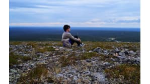 Nainen istuu tunturin laella ihailemassa maisemia