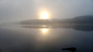 Sumuinen auringonnousu veden yllä