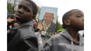 Kaksi mustaihoista lasta, joiden takaa näkyy jättikokoinen maalaus Nelson Mandelasta.