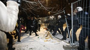 Riehuvia mellakoitsijoita repii aitaa alas, poliiseja toisella puolella.