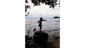 Tyttö tasapainoilee kivellä järven rannalla