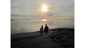 Nainen ja mies rantakalliolla auringon laskiessa