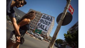 Nuori pari kävelee trendikästä Long street -katua pitkin Etelä-Afrikan Kapkaupungissa. Toisella puolen katua on jättimäinen juliste, jossa lukee ytimekkäästi: "Zuma must fall".