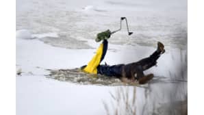 Pilkkijä pitelee kairaa osittain veden alle vajonneena jäiden keskellä.