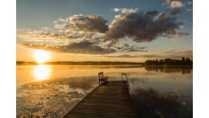 Laituri järven rannassa. Aurinko metsänrajassa, järvi on kuin peilityyni.