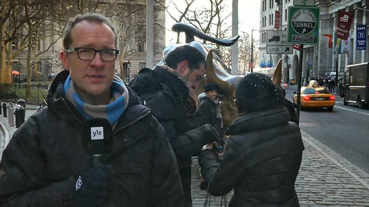 Kirjeenvaihtaja Christian Vuojärvi puhuu kameralle. Taustalla yhdysvaltalainen suurkaupungin katu. Kolme ihmistä suunnittelee toistensa snapshot-kuvaamista.