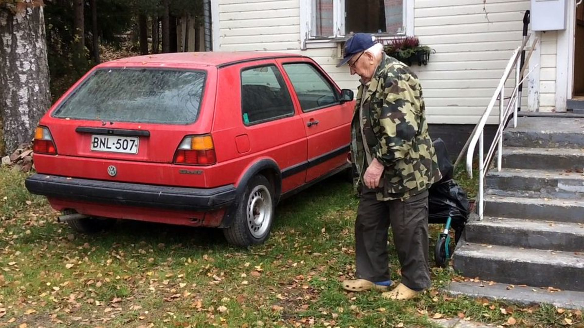 Maastopukuinen mies on menossa omakotitalon edessä odottavaan punaiseen autoon.